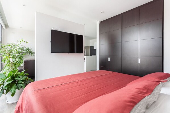 Une chambre moderne avec un grand lit, un téléviseur à écran plat fixé au mur et une armoire sombre.