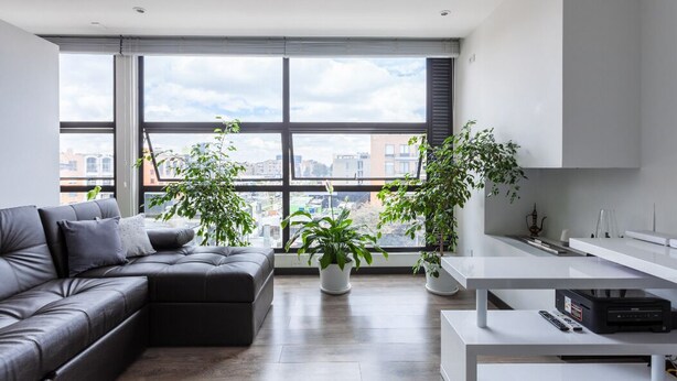 Una sala de estar moderna con un sofá seccional, una mesa de centro blanca y grandes ventanales con vistas a la ciudad.