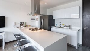 Una cocina moderna con una isla central, armarios blancos, electrodomésticos de acero inoxidable y una puerta oscura.