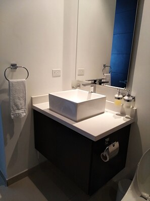 Une salle de bain moderne avec un lavabo blanc, un meuble sombre et un grand miroir.