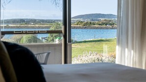 Een kamer met een groot raam met uitzicht op een waterpartij, een grasveld en een heuvel in de verte.
