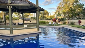 Una piscina con un gazebo, poltrone a sdraio e vegetazione tropicale.