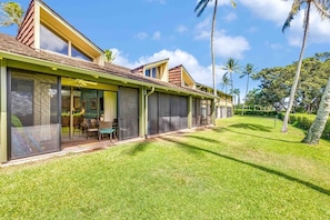 A modern house with large sliding glass doors, a patio with outdoor furniture, and a well-maintained lawn.