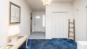 Een hal met een blauw tapijt, een witte deur, een houten ladder en een lijst met een foto aan de muur.