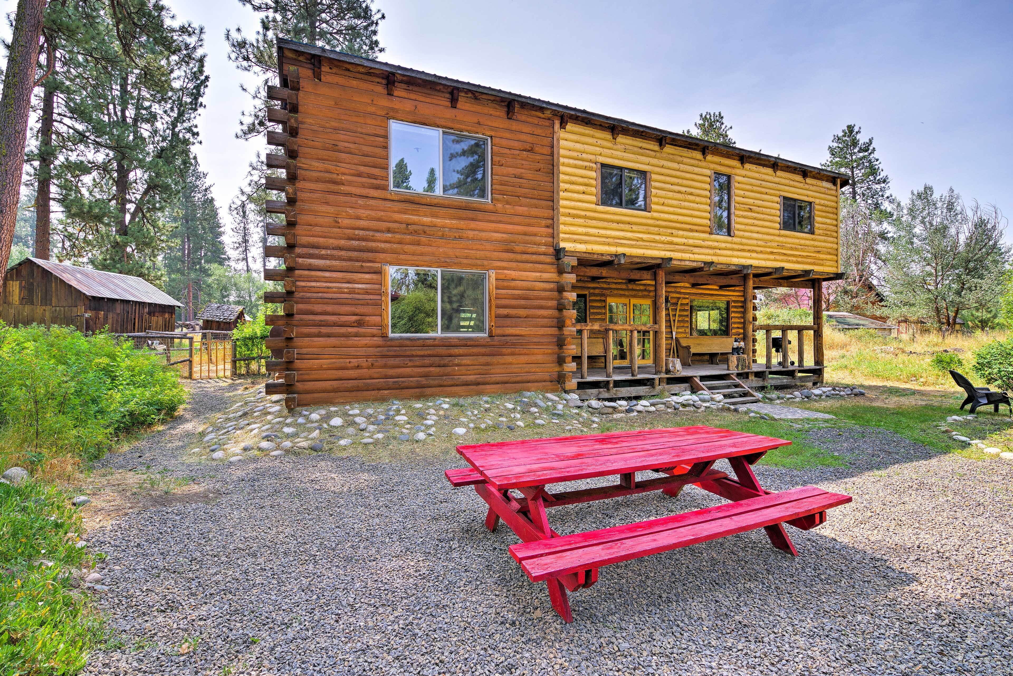 A two-story log cabin with a porch and a red picnic table in front.