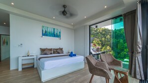 A modern bedroom with a large bed, a desk, and a chair, a painting on the wall, and a balcony with a view of greenery. - The  new luxury architect modern villa in  Haad Yao  with huge amazing seaview. (Ko Pha Ngan)