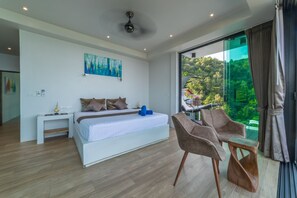 A modern bedroom with a large bed, a desk, and a chair, a painting on the wall, and a balcony with a view of greenery. - The  new luxury architect modern villa in  Haad Yao  with huge amazing seaview. (Ko Pha Ngan)
