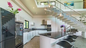 A modern kitchen with a central island, stainless steel appliances, and a staircase leading to an upper level. - The  new luxury architect modern villa in  Haad Yao  with huge amazing seaview. (Ko Pha Ngan)
