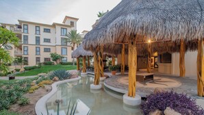 Un complexe hôtelier doté d’une piscine, de bâtiments à toits de chaume et d’un immeuble avec de nombreux balcons.