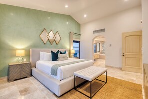 Un dormitorio moderno con una cama grande, mesitas de noche, un banco y vistas al baño.