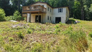 Una casa de dos pisos con un balcón, rodeada de un bosque frondoso.