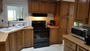 Una cocina con armarios de madera, estufa negra, microondas y pileta.