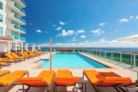 A pool area with lounge chairs and a view of the ocean.