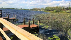 A wooden dock extending into a body of water with lily pads and reeds.