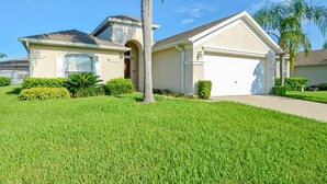 A single-story house with a garage, a well-maintained lawn, and a palm tree.