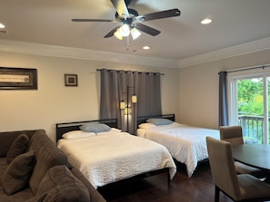 A bedroom with two beds, a ceiling fan, a window with a view, and a dining table with chairs.