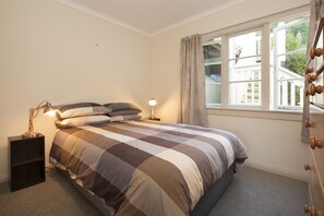 A bedroom with a bed, bedside table, lamp, and a window with curtains. - Escape North - Extended Family Retreat, located in central Russell (Russell)