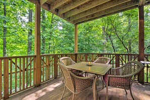 A covered wooden deck with wicker furniture and a table, surrounded by a wooden railing, overlooking a forested area. - Beautiful Condo in the Mountain Air Community (Burnsville)