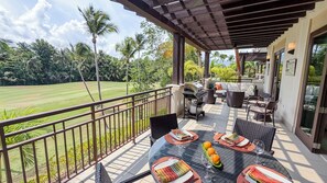 An outdoor patio with a dining table set for four, surrounded by wicker furniture, a grill, and a view of a lush green landscape. - veElegant Villa, Pool, Golf Cart, Beach & Resort Amenities. Secure & Relaxing (Río Grande)