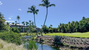 A golf course with a pond, palm trees, and a building with a sloped roof. - veElegant Villa, Pool, Golf Cart, Beach & Resort Amenities. Secure & Relaxing (Río Grande)