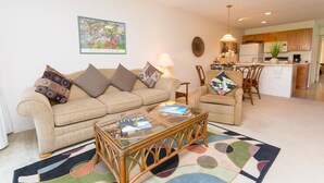 A living room with a sofa, coffee table, and chairs. There is a kitchen in the background. - Hale Kamaole 141 Ground floor condo, easy access to best beach on Maui! (Kihei)