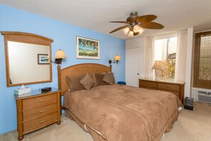 A bedroom with a large bed, a ceiling fan, two bedside tables with lamps, a dresser, and a window with curtains.
