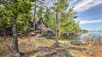 A cabin by a lake with a dock extending into the water, surrounded by trees and rocky terrain.