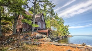 Un chalet rustique aux murs en bois, situé au bord d’un lac, avec une jetée qui s’avance dans l’eau.
