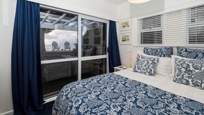 Ein Schlafzimmer mit großem Fenster, einem Bett mit gemusterten Betttextilien und Blick aufs Meer.