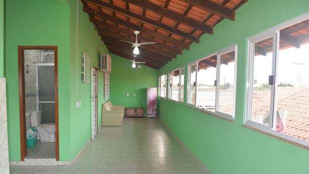 Un corridoio con pareti verdi, pavimento piastrellato e una ventola a soffitto. Sulla destra si vedono delle finestre e, a sinistra, una porta.