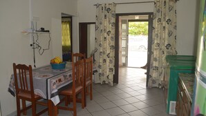 Zona pranzo con tavolo apparecchiato per quattro persone, sedie, una ciotola di frutta e un telefono fissato al muro.