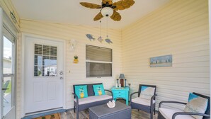 A room with a white door, a ceiling fan, two wicker chairs with cushions, a small table with a lamp, and a wall-mounted painting. - The Villages 2BR Vacation Home, Lanai & Golf Cart (The Villages)