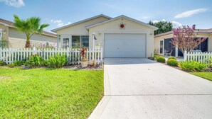 A single-story house with a garage, a front yard with a white picket fence, and a palm tree. - The Villages 2BR Vacation Home, Lanai & Golf Cart (The Villages)