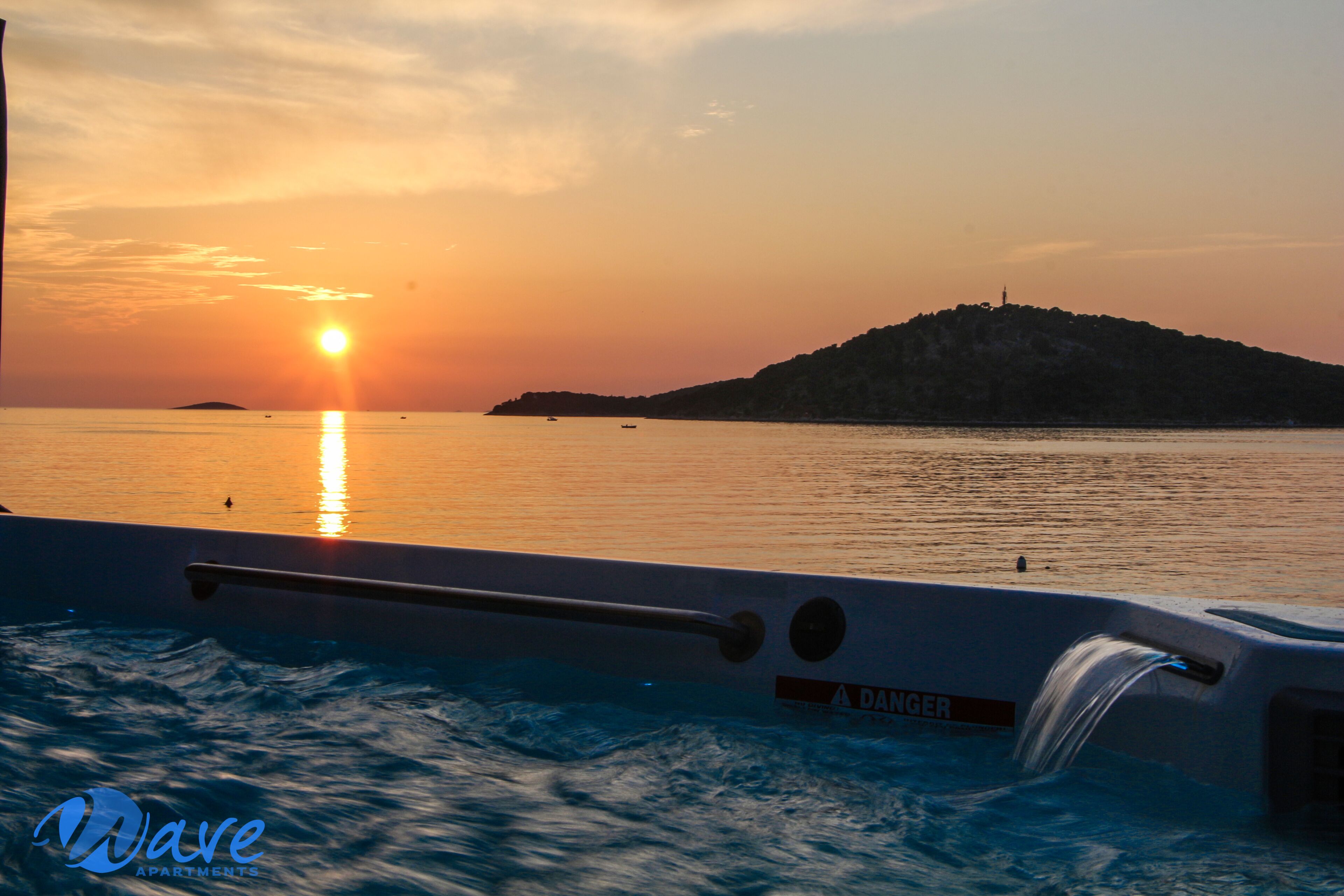 A sunset view from a boat with a "DANGER" sign, calm water, and a distant island.