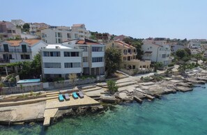 A coastal residential area with clear blue waters, a swimming pool, and modern multi-story buildings.