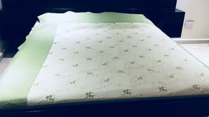 Ein ordentlich bezogenes Bett mit einer grün-weißen Blumensteude, einem dunklen Kopfteil und einem kleinen Nachttisch mit einer Tasse.