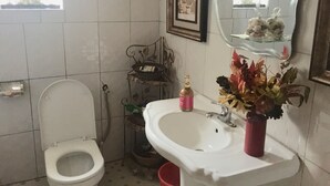 Ein Badezimmer mit Toilette, Waschbecken und Dekoration, darunter ein gerahmtes Bild und eine Vase mit Blumen.