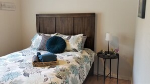 Una cama bien hecha con una colcha floral, una almohada azul oscuro y una cesta tejida con mantas dobladas.