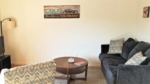 Una sala de estar con televisor, sofá, mesa de centro y un adorno de pared.