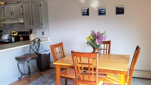 Un comedor con una mesa y sillas de madera, un jarrón con flores, y una cocina al fondo.