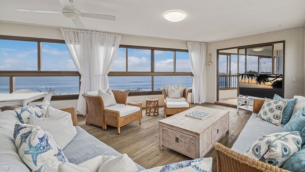 A spacious living room with a view of the ocean, featuring wicker furniture, a wooden coffee table, and large windows. - Parkyn Place 6 - Three Bedroom Oceanview Apartment on Mooloolaba Spit (Mooloolaba)