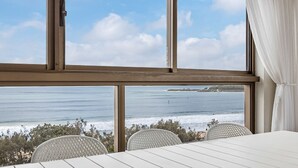 A room with a large window overlooking the ocean, a white table, and two white chairs. - Parkyn Place 6 - Three Bedroom Oceanview Apartment on Mooloolaba Spit (Mooloolaba)