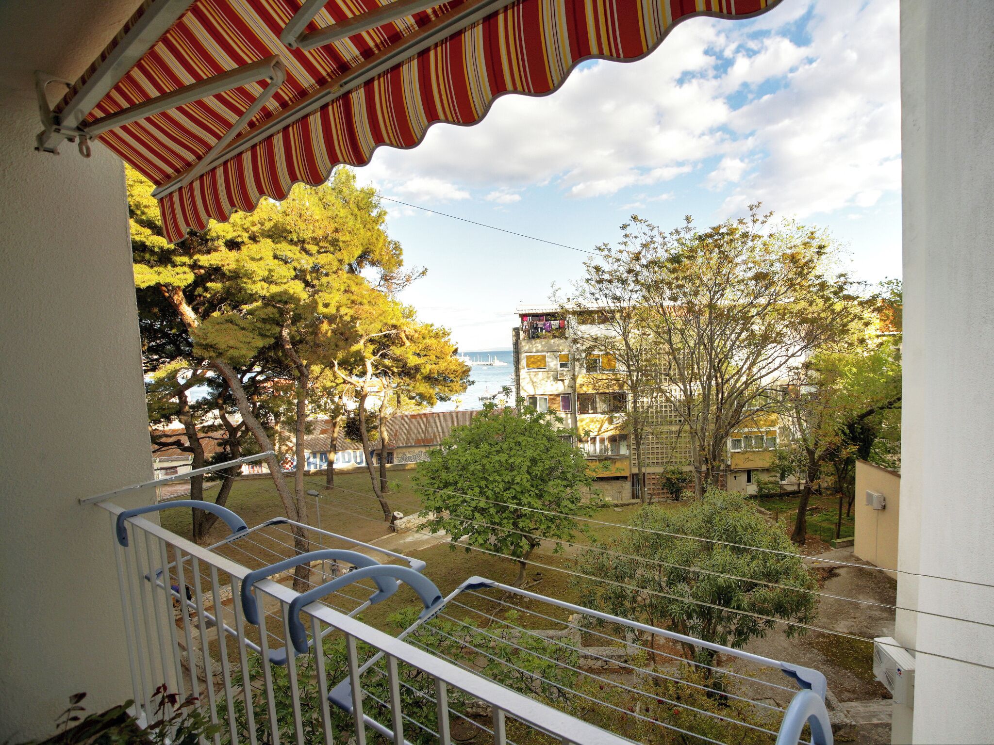 A balcony with a striped awning overlooking a residential area with trees and buildings.