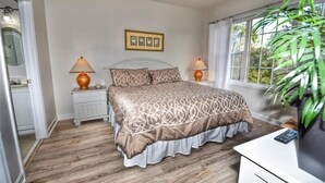 Ein Schlafzimmer mit einem Bett, zwei Nachttischlampen, einem Deckenventilator, einem Fenster mit Vorhängen und einer Pflanze.