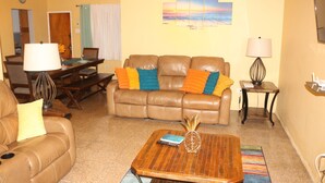 A living room with a brown leather sofa, a wooden coffee table, and a dining area with a table and chairs. - ★ Cozy Kingston Getaway ★ Relaxing, Quaint & Centrally Located ★ (Kingston 10)