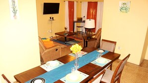 A dining area with a long wooden table set for two, a blue table runner, and a vase with yellow flowers. - ★ Cozy Kingston Getaway ★ Relaxing, Quaint & Centrally Located ★ (Kingston 10)