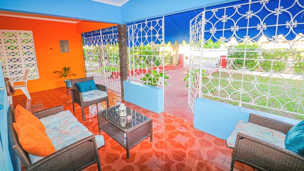A brightly colored room with orange and blue walls, wicker furniture, and a glass coffee table. - ★ Cozy Kingston Getaway ★ Relaxing, Quaint & Centrally Located ★ (Kingston 10)