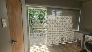 A room with a sliding glass door leading to a balcony, a washing machine, and a chair. - ★ Cozy Kingston Getaway ★ Relaxing, Quaint & Centrally Located ★ (Kingston 10)