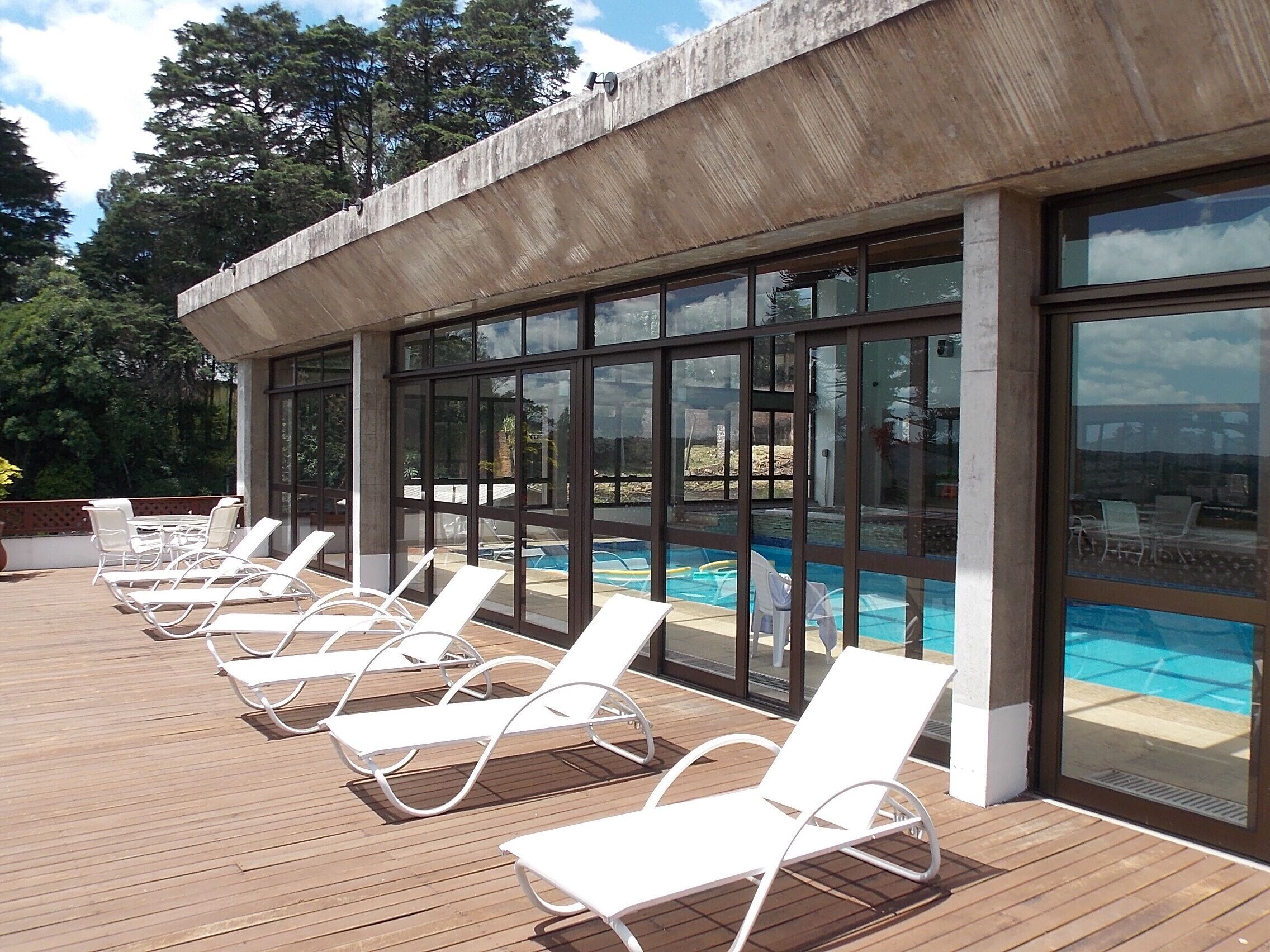 Zona de piscina con sillones blancos y vista al agua a través de amplios ventanales.