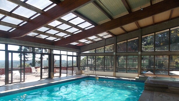 Une piscine intérieure à l’eau d’un bleu limpide, dotée de grandes fenêtres et d’un plafond en bois.